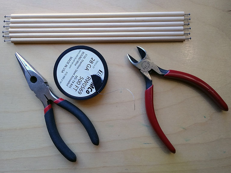 Photograph of the tools and materials needed to build the described tensegrity models: 1/4" wood dowel cut to length with small box nails at either end; spool of 28 gauge stainless steel wire; needle nose pliers; wire cutters.