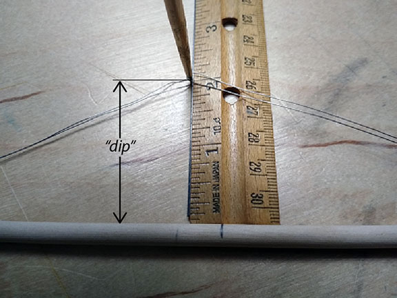 Photograph of a strut with its wire tendons being measured for accuracy using height of the triangle formed by the strut, one long, and one short tendon.
