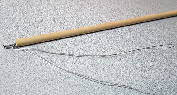 Photograph of a 1/4" by 9" wood dowel strut to be used in building the tensegrity models, with wire tendon loops attached to either end.