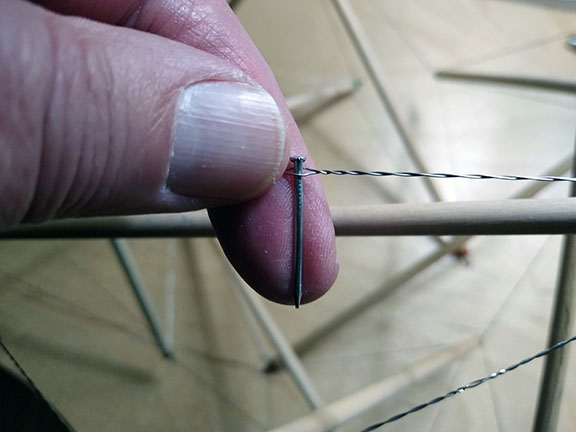 Photograph of a wire tendon loop in a tensegrity sphere being tightened by twisting, using a small nail as a lever.
