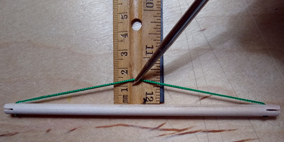 Photograph of a strut with its tendon sling extended over a ruler and showing a 1.25 cm dip for the model of the 30-strut tensegrity icosahedron.
