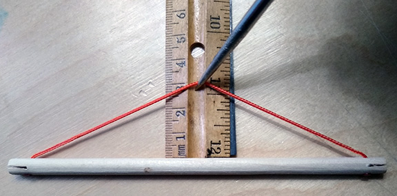 Photograph of a strut with its tendon sling extended over a ruler and showing a 3 cm dip for the model of the 6-strut tensegrity tetrahedron.